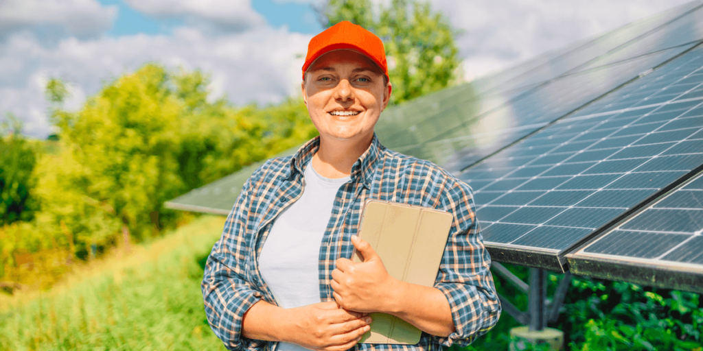 Farmer using a tablet for REAP Grant Application Process research by photovoltaic solar panels, symbolizing green technology and eco-friendly agriculture.